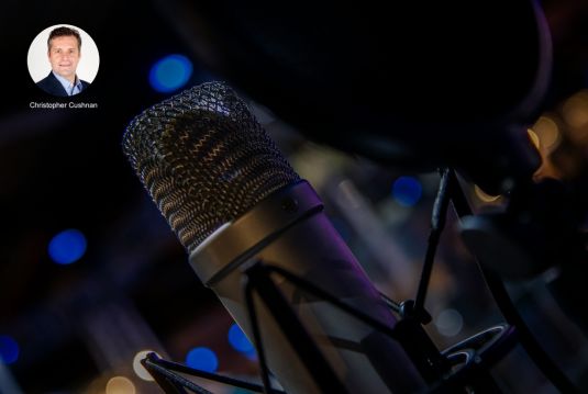 Microphone with a dark background, top right of the picture is a photo of a man, Christopher Cushnan