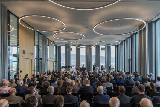 Raum voller Leute mit Podium, Blick über Publikum