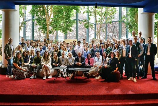 Group photo of all participants posing in front of a window on a red carpet