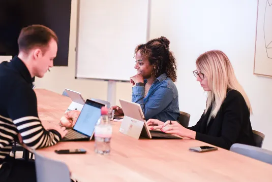 Three people are working on their laptops at a table.