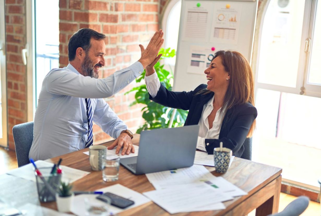 A business man and woman give each other a high-five and laugh.