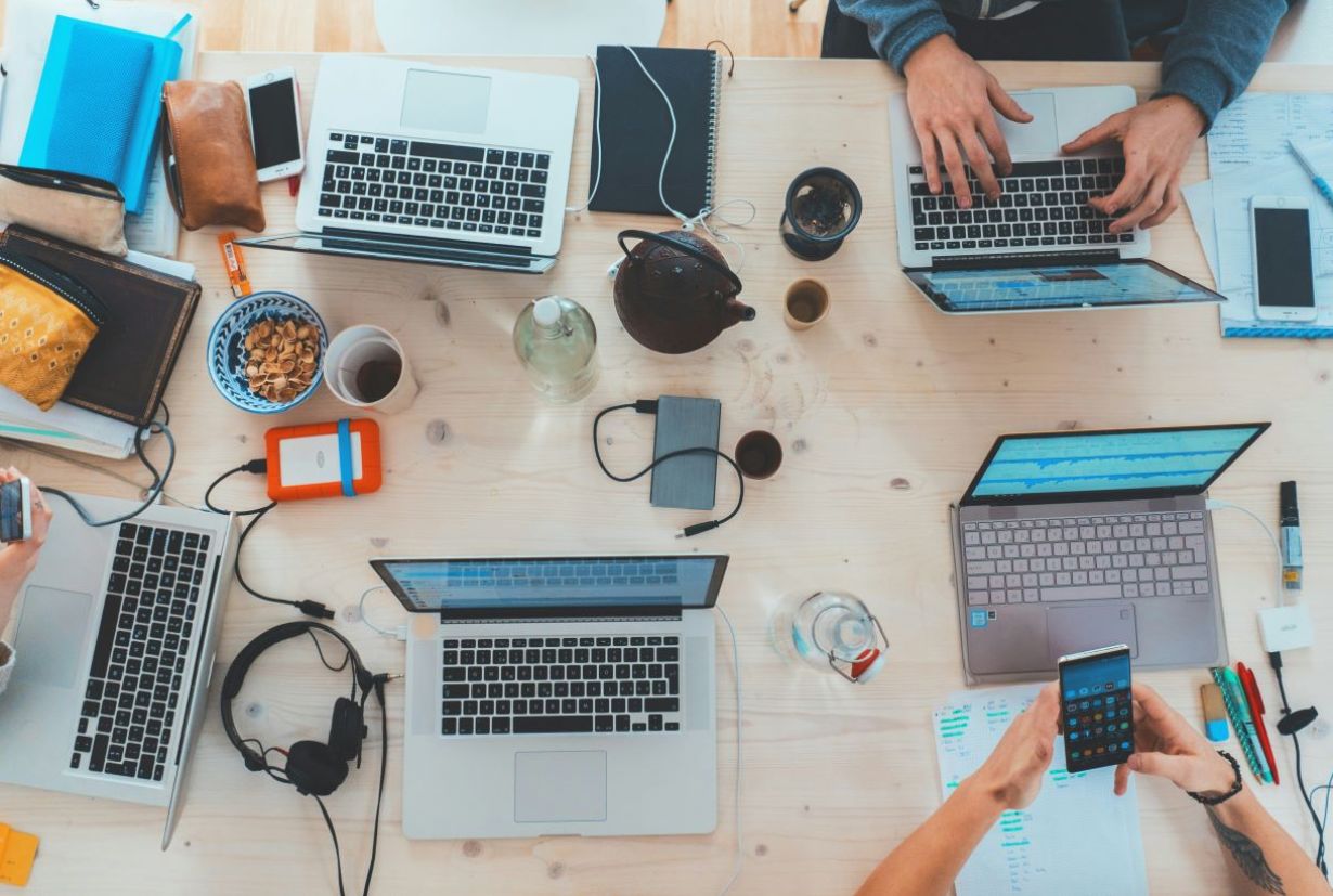 Ein Tisch von oben mit vielen Personen die an Laptops arbeiten.